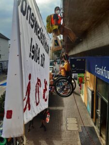 Von der seite aufgenommen, hinter dem Banner, man siet von der seiten ein Rollstuhlfahrer im Seil