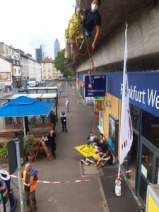 Banner von der Seite in der Luft aufgenommen, unten Menschen, ein Mensch hat sich auf einer Isomatte hingelegt