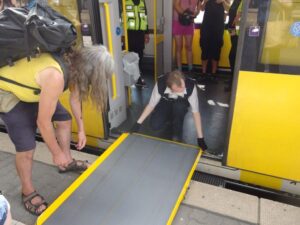 Am Bahnsteig vor der geöffneten Zugtür, ein Mensch von der Bahn legt eine Rampe an