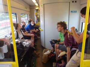 Zugabteil mit der Gruppe, davon 3 Menschen in Rollstühlen, weitere Menschen und das WC. Ganz schön eng!